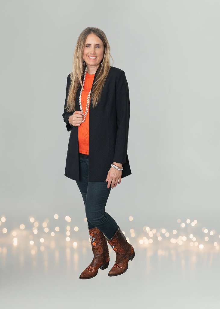 Dr. Sarah Diamond smiling, wearing an orange top and black blazer, seated for a professional portrait.